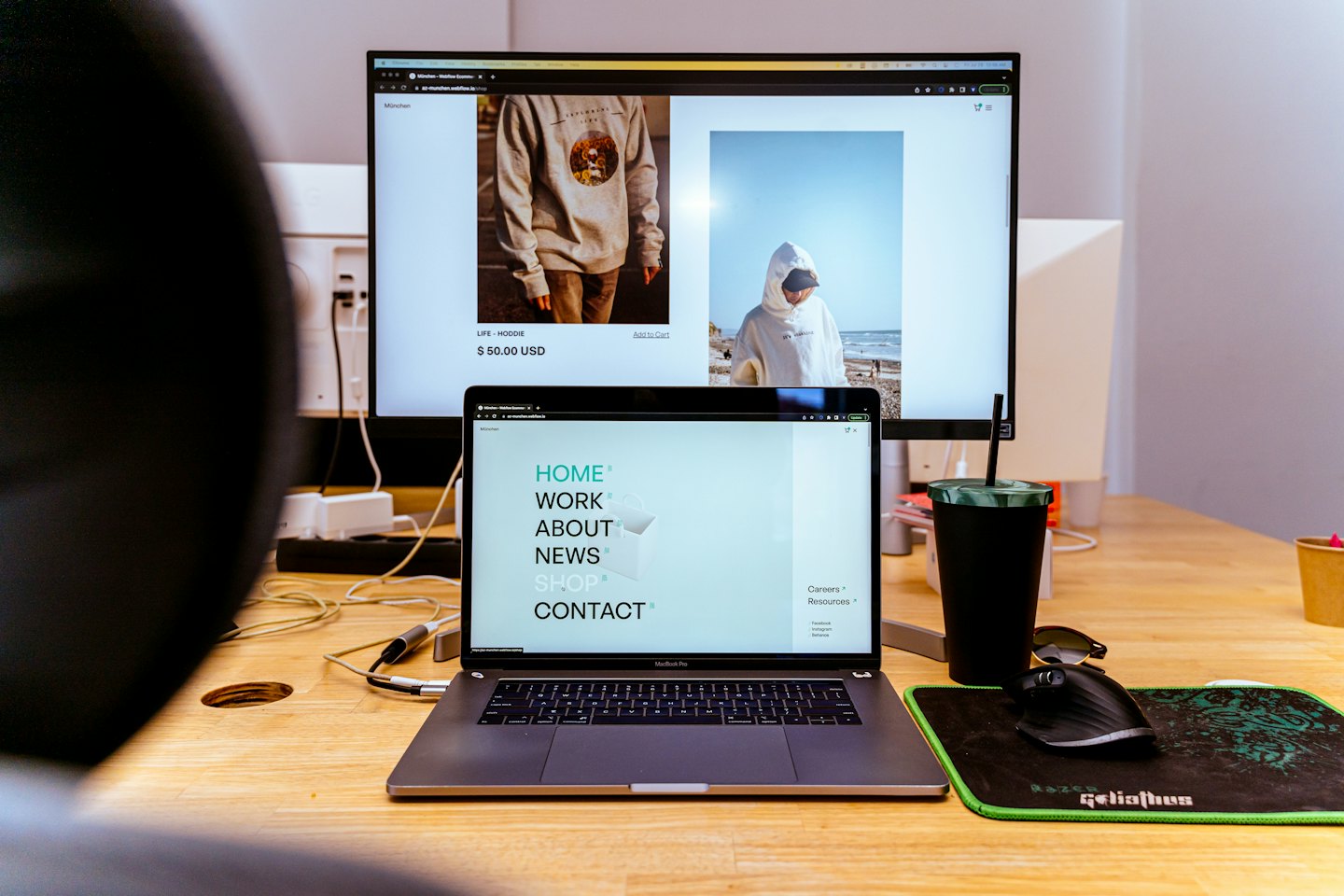Person working on laptop and monitor displaying e-commerce website.
